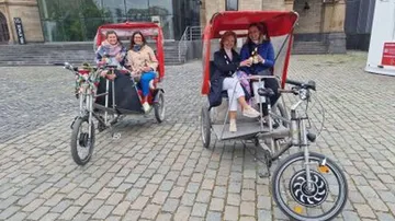 Personen sitzen in Fahrradtaxis draußen.