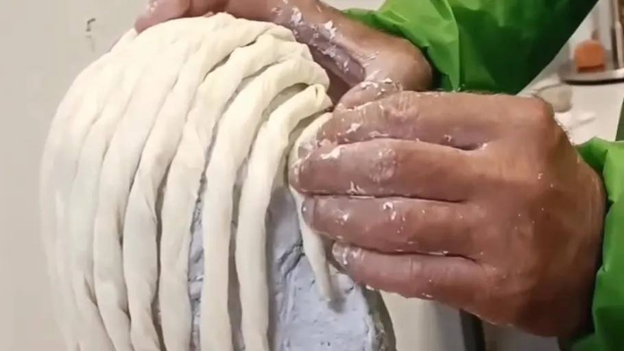 Hände formen Tonstreifen auf einem Kopf.