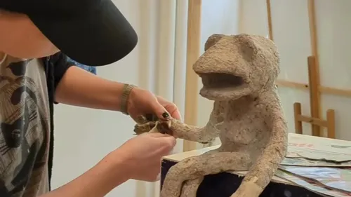 Person sculpting a smiling creature sculpture indoors.