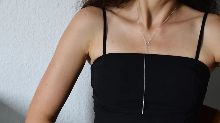 Woman wearing black dress and necklace indoors.