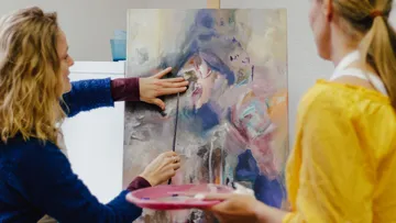 Woman points at painting in art class.