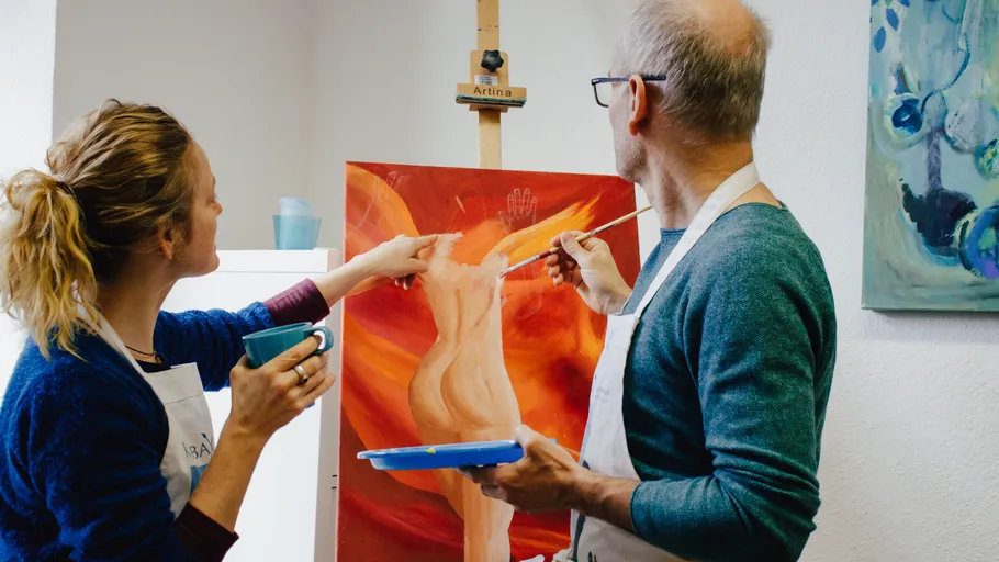 Two people painting on a canvas indoors.