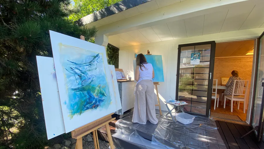 Woman painting outside studio beside easels.