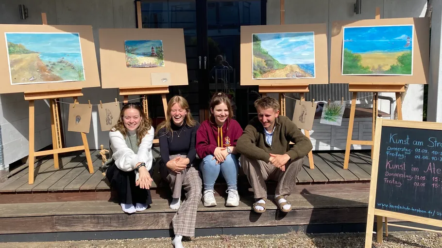 Four people sitting in front of displayed paintings.
