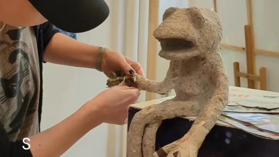 Person crafting a frog sculpture indoors.