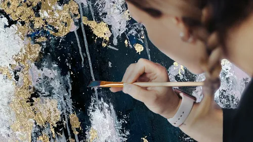 Person painting abstract art with gold accents.