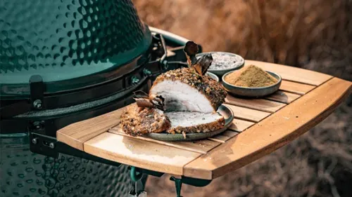 Grilled pork on wooden tray near smoker.