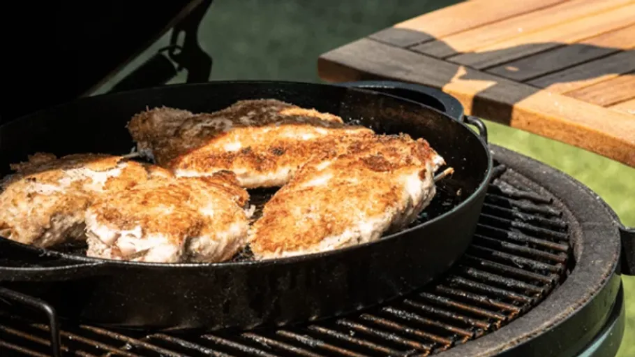 Chicken frying on grill with wooden table.