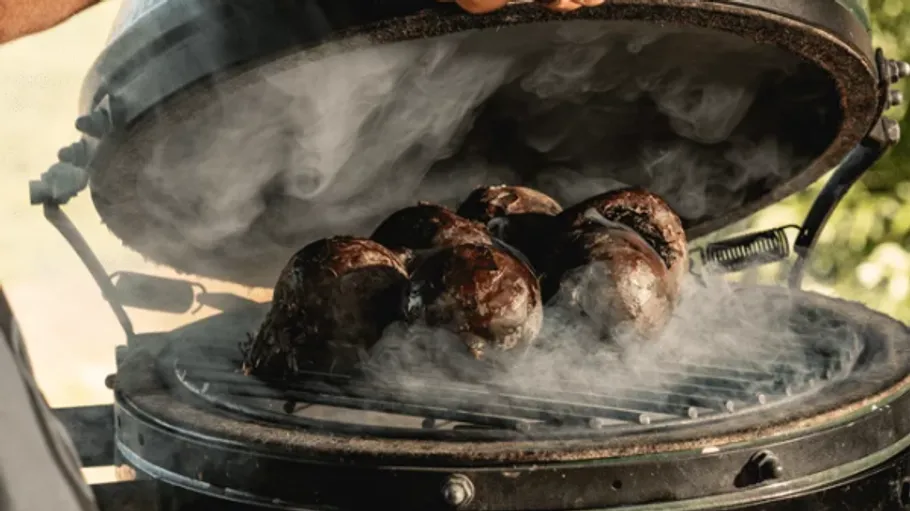 Grill with mushrooms releasing smoke outdoors.