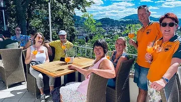 Gruppe genießt Getränke auf sonnigem Balkon.