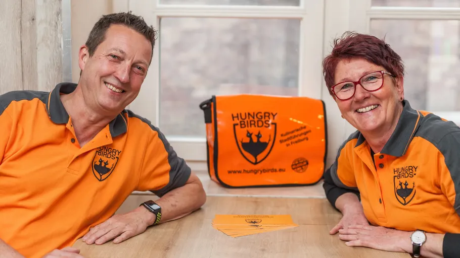 Two smiling people wearing orange shirts indoors.