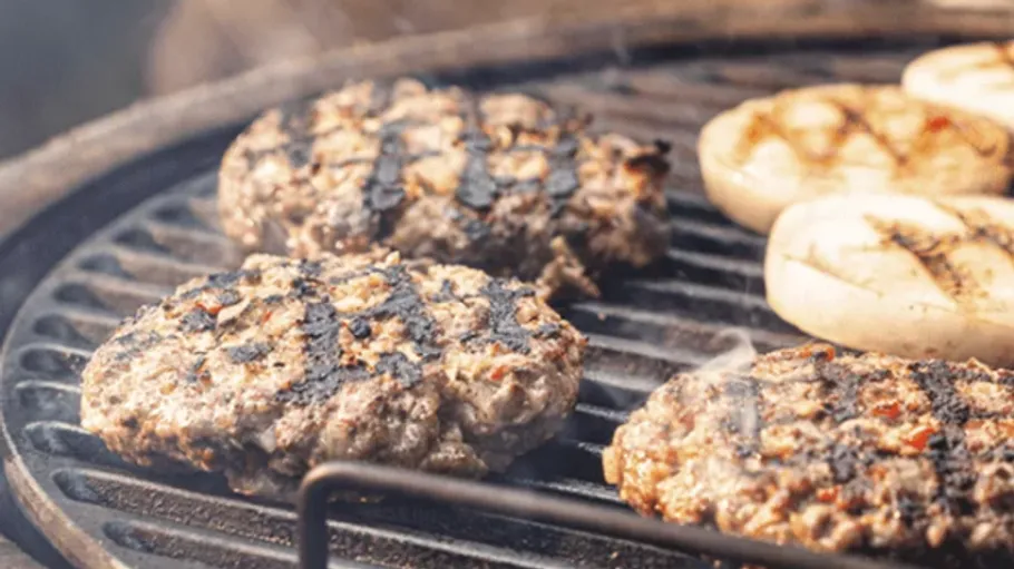 Burgers and buns grilling on a barbecue.