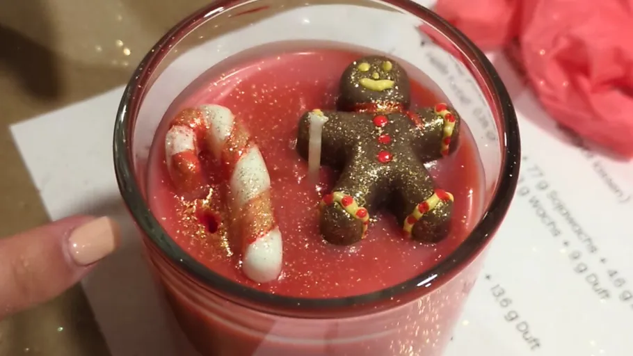 Gingerbread figure on red candle inside glass.