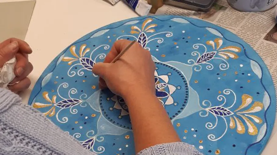 Person painting intricate design on round object.