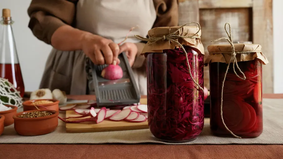 Person slicing vegetables next to pickled jars.