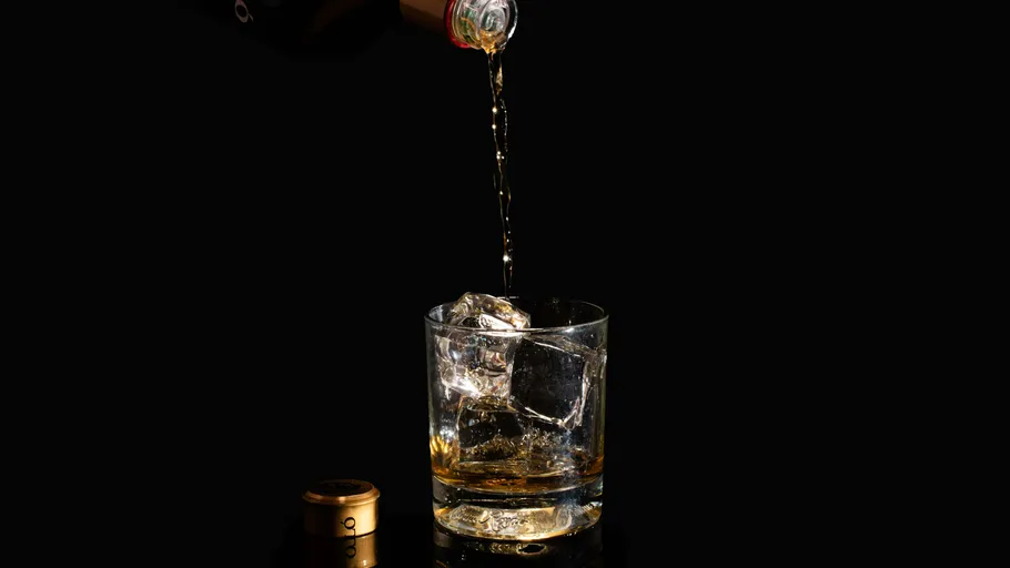 Liquor pouring into glass with ice cubes.
