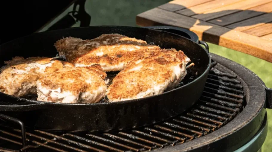 Chicken breasts frying in a cast iron pan outdoors.