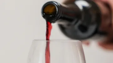 Rotwein wird in Glas gegossen, verschwommener Hintergrund.