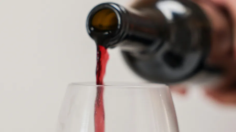 Red wine pouring into glass, blurred background.
