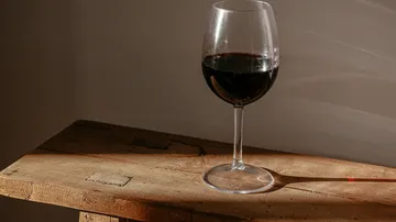 Weinglas mit Rotwein auf Holztisch.