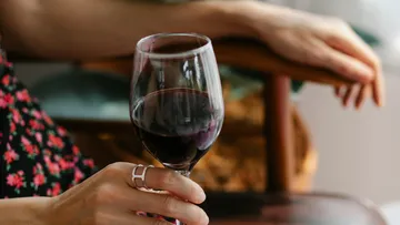 Person hält Weinglas, sitzt drinnen.