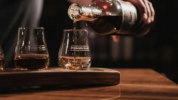 Person gießt Whiskey in Glas auf Holz.