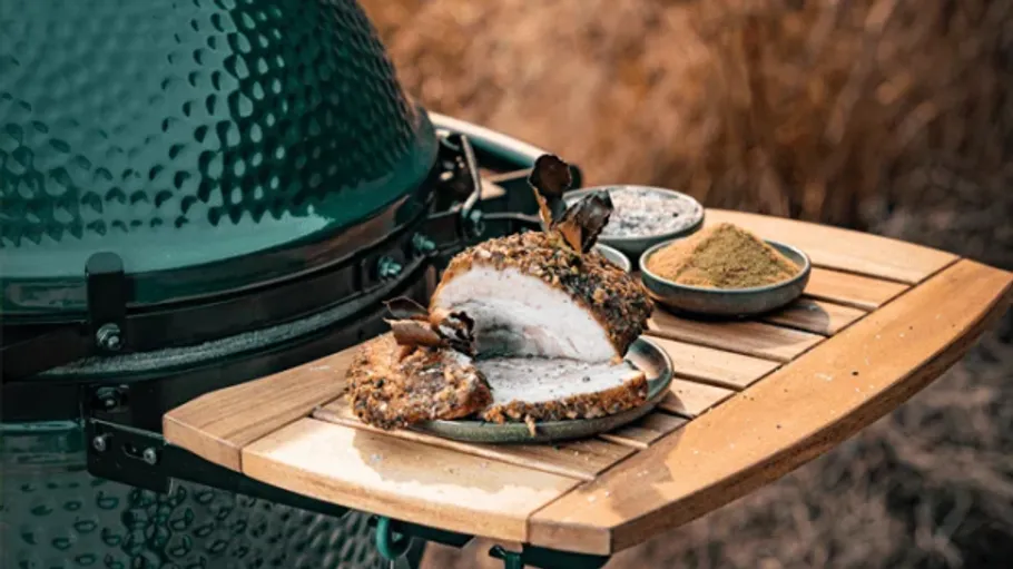 Grilled meat on wooden side table near grill.