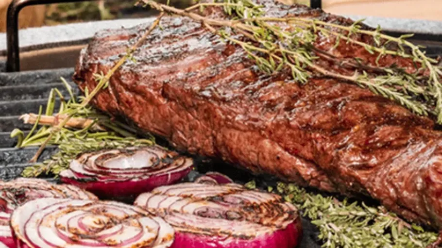 Grilled steak and onions with herbs on grill.