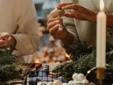 Hands decorate a table with Christmas decorations and candles.