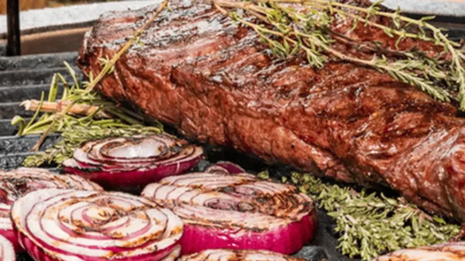 Grilled steak and onions with herbs on grill.