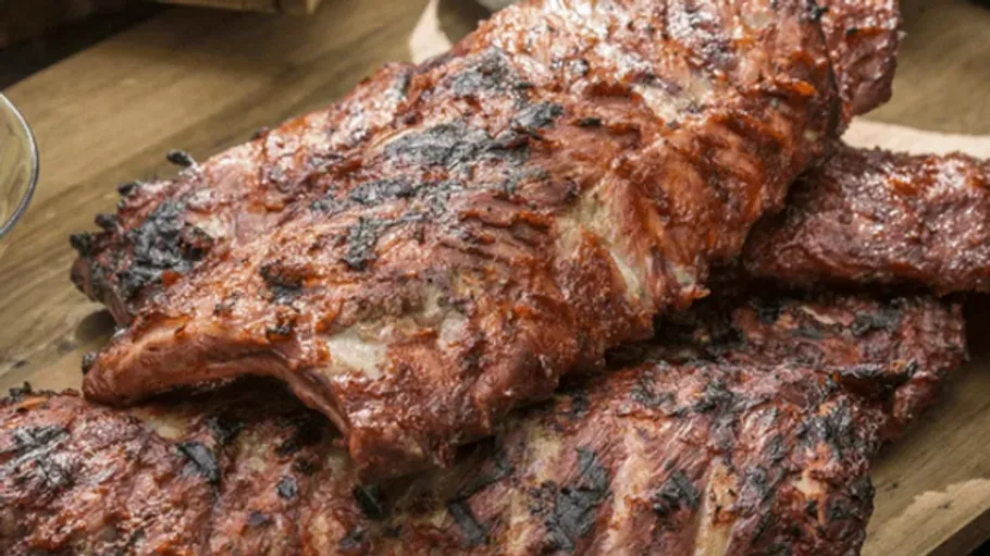 Grilled ribs stacked on wooden table.