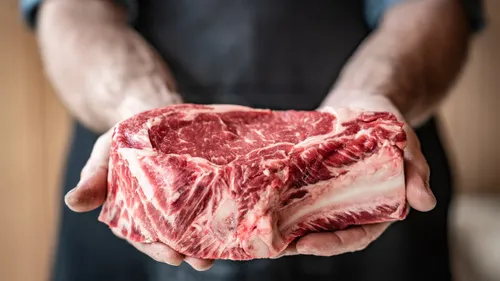 Person hält rohes Steak, trägt Schürze.