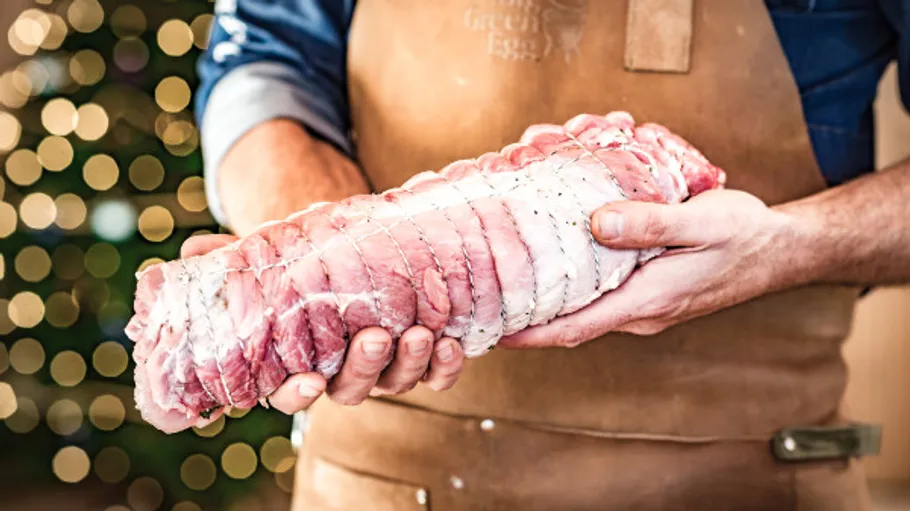 Person holding tied raw meat roast indoors.