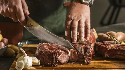 Mann schneidet Steak auf Holzbrett.