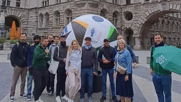 Gruppe posiert mit Fußball auf historischem Platz.