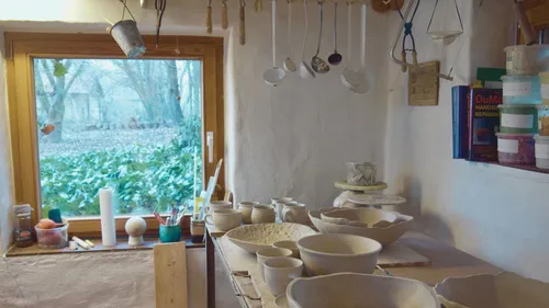 Pottery studio with tools and ceramics by window.