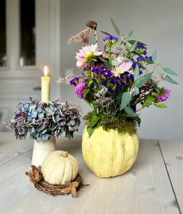 Floral arrangement in pumpkin vase, candle beside.