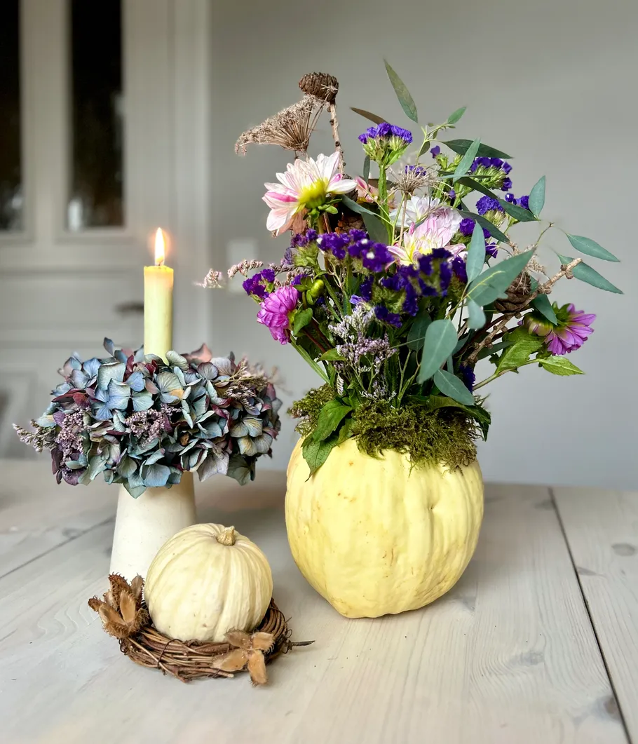Floral arrangement in pumpkin vase, candle beside.
