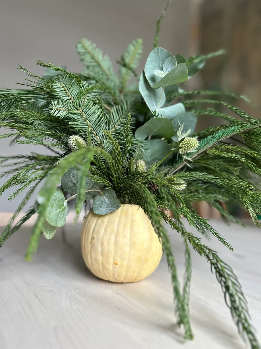 Pumpkin vase with green foliage arrangement indoors.