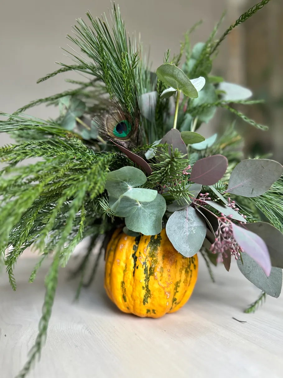 Pumpkin vase with greenery and leaves arrangement.