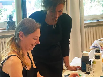 Two women smiling while painting indoors.