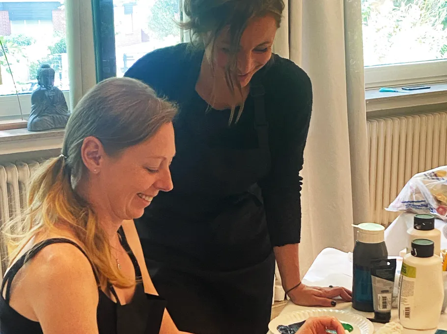 Two women smiling while painting indoors.