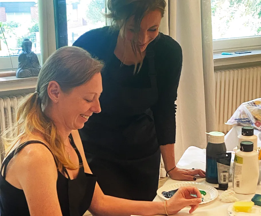 Two women painting indoors, smiling.