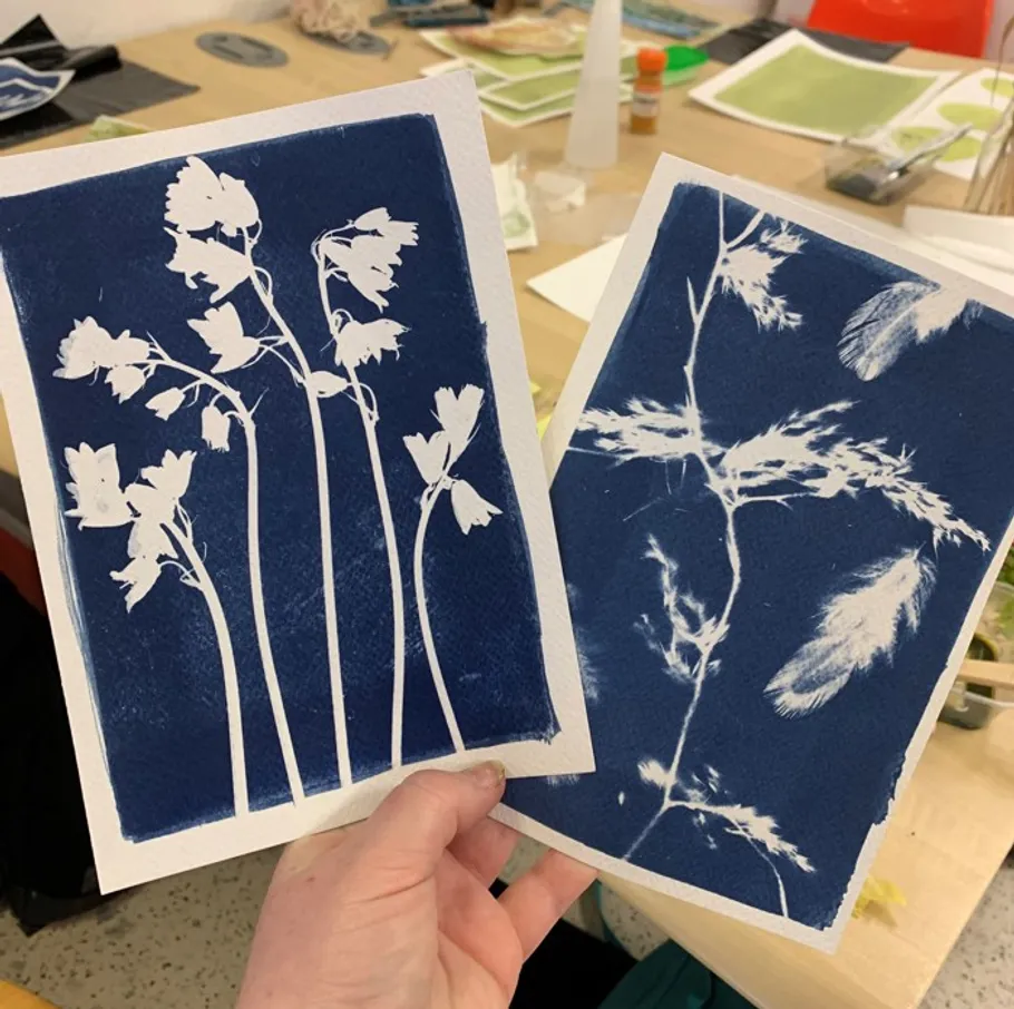 Hand holding two cyanotype prints of plants.
