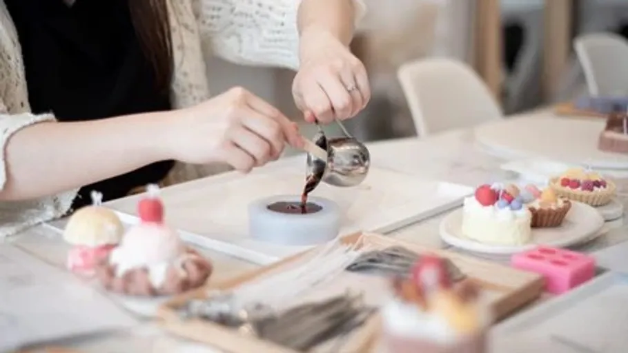 Person pours chocolate in mold on table.