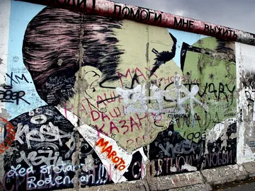 Graffiti-Wand zeigt zusammenstoßende Porträts mit vielen Schriftzügen.