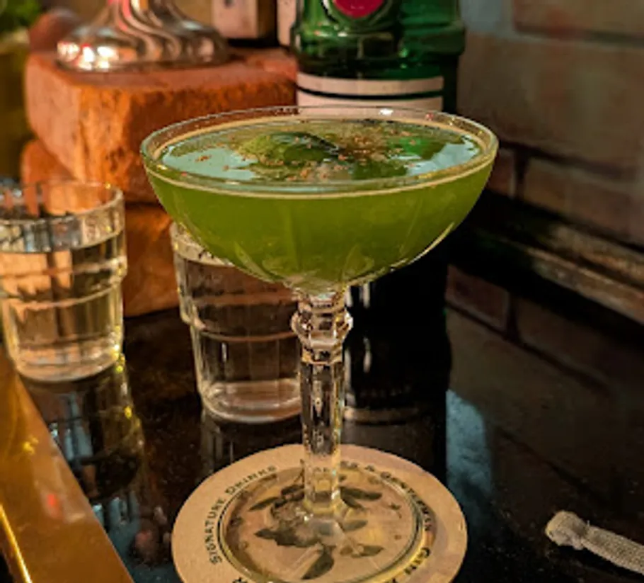 Green cocktail in glass on bar counter.