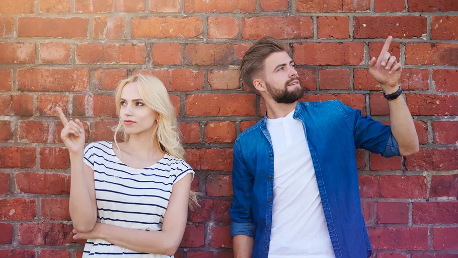 Man and woman point up against brick wall.