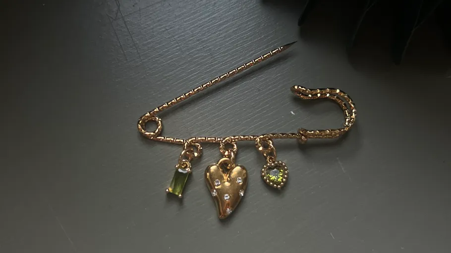 Goldene Brosche mit Herzanhängern auf Tisch.