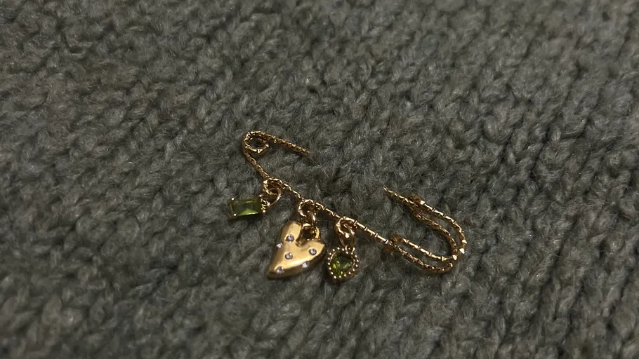 Golden earring with heart charm on fabric.